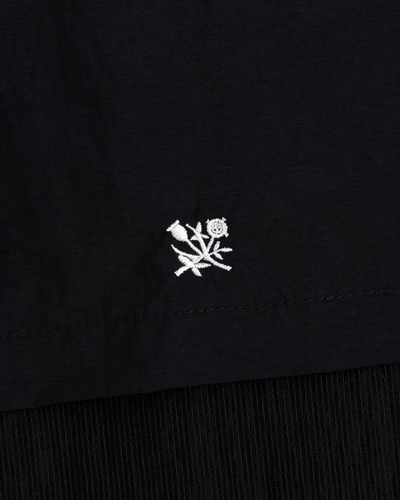 Small white embroidered rose with leaves on black Nylon Track Jacket, near the hem.