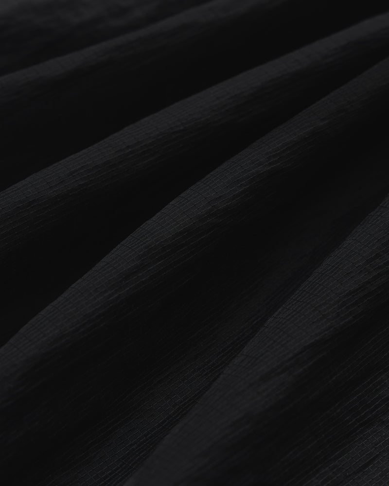 Close-up of black Nylon Track Jacket fabric with a textured, slightly ridged surface and soft, diagonal folds.