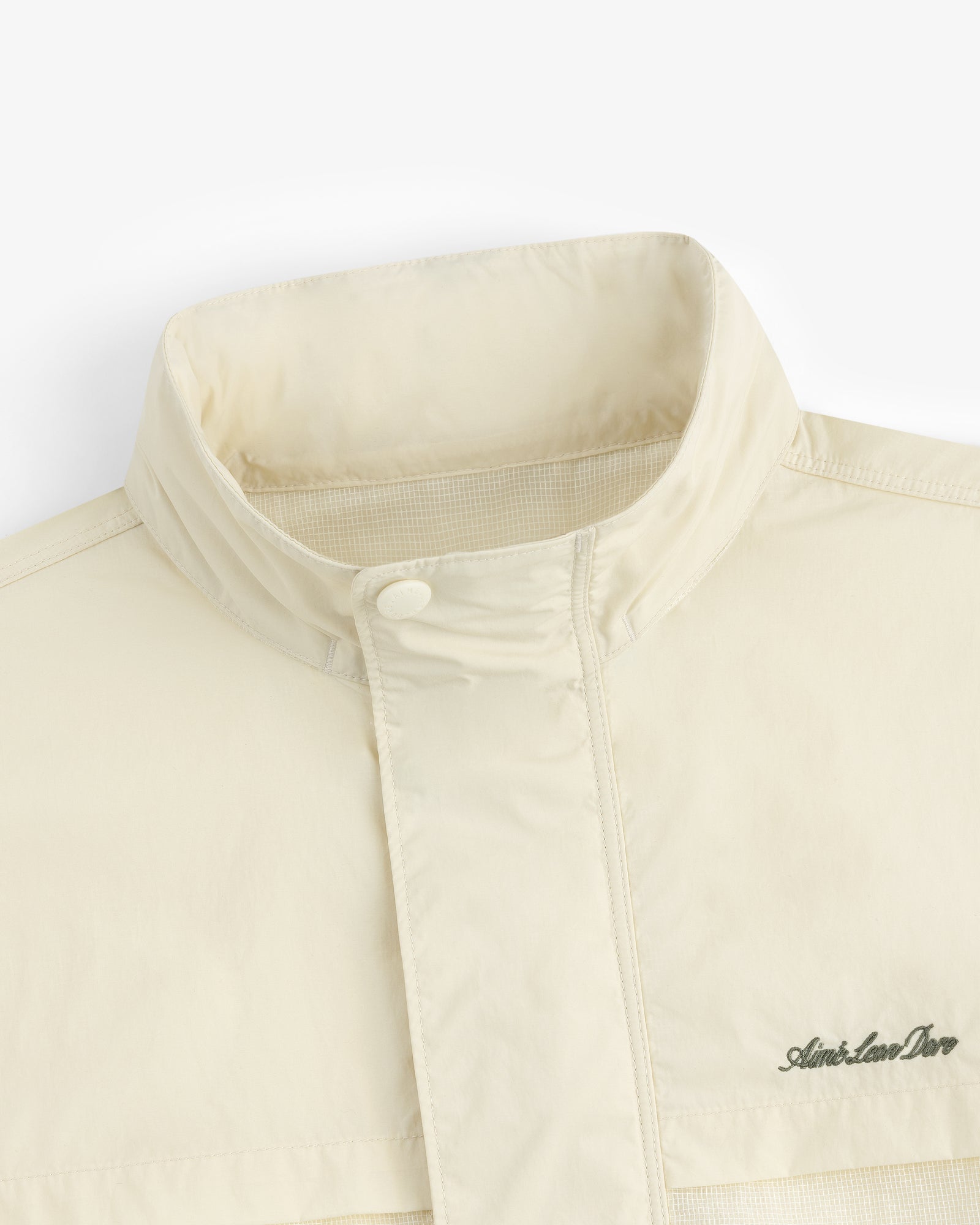 Close-up of the Nylon Track Jacket in cream, featuring a high collar and the Aimé Leon Dore logo embroidered on the chest.