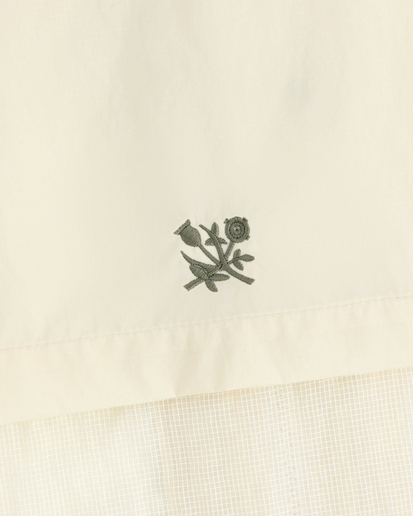 Green floral embroidery on cream nylon track jacket featuring a subtle checked pattern below.