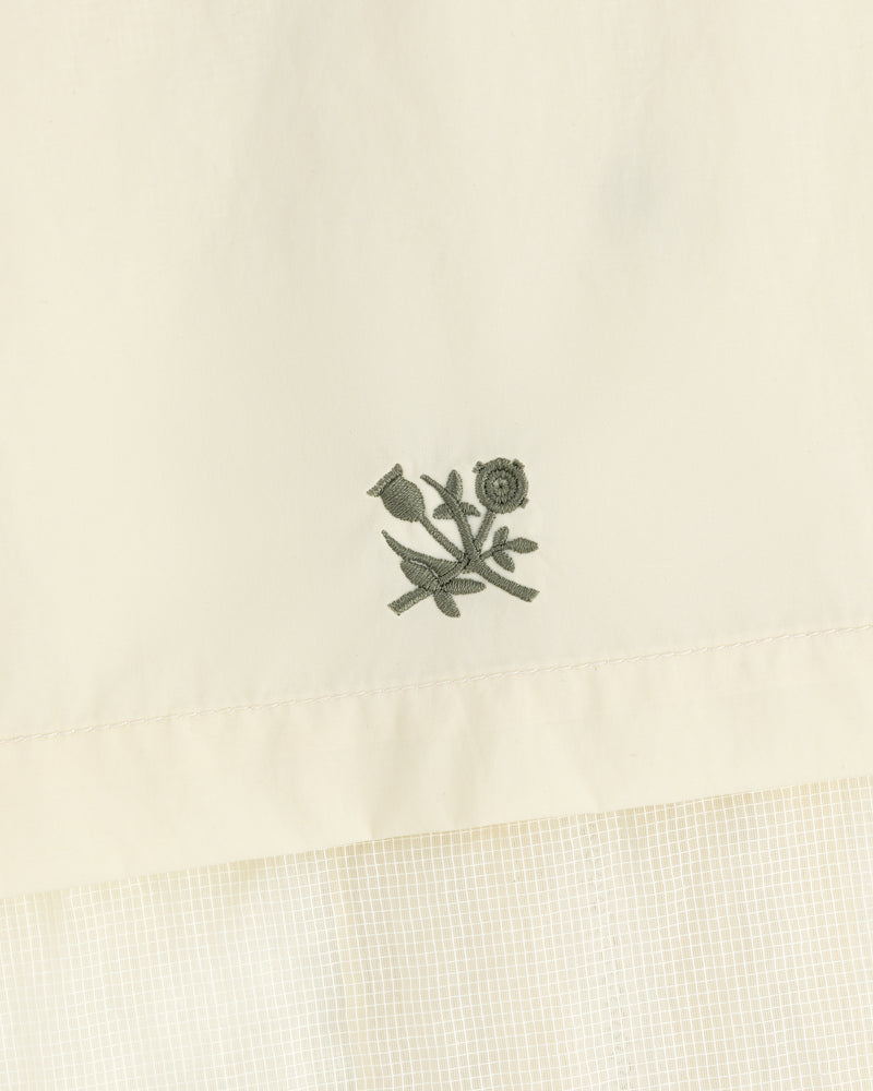 Green floral embroidery on cream nylon track jacket featuring a subtle checked pattern below.