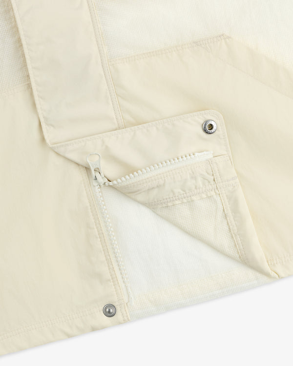 Close-up of a cream-colored Nylon Track Jacket featuring a zippered pocket and snap buttons.