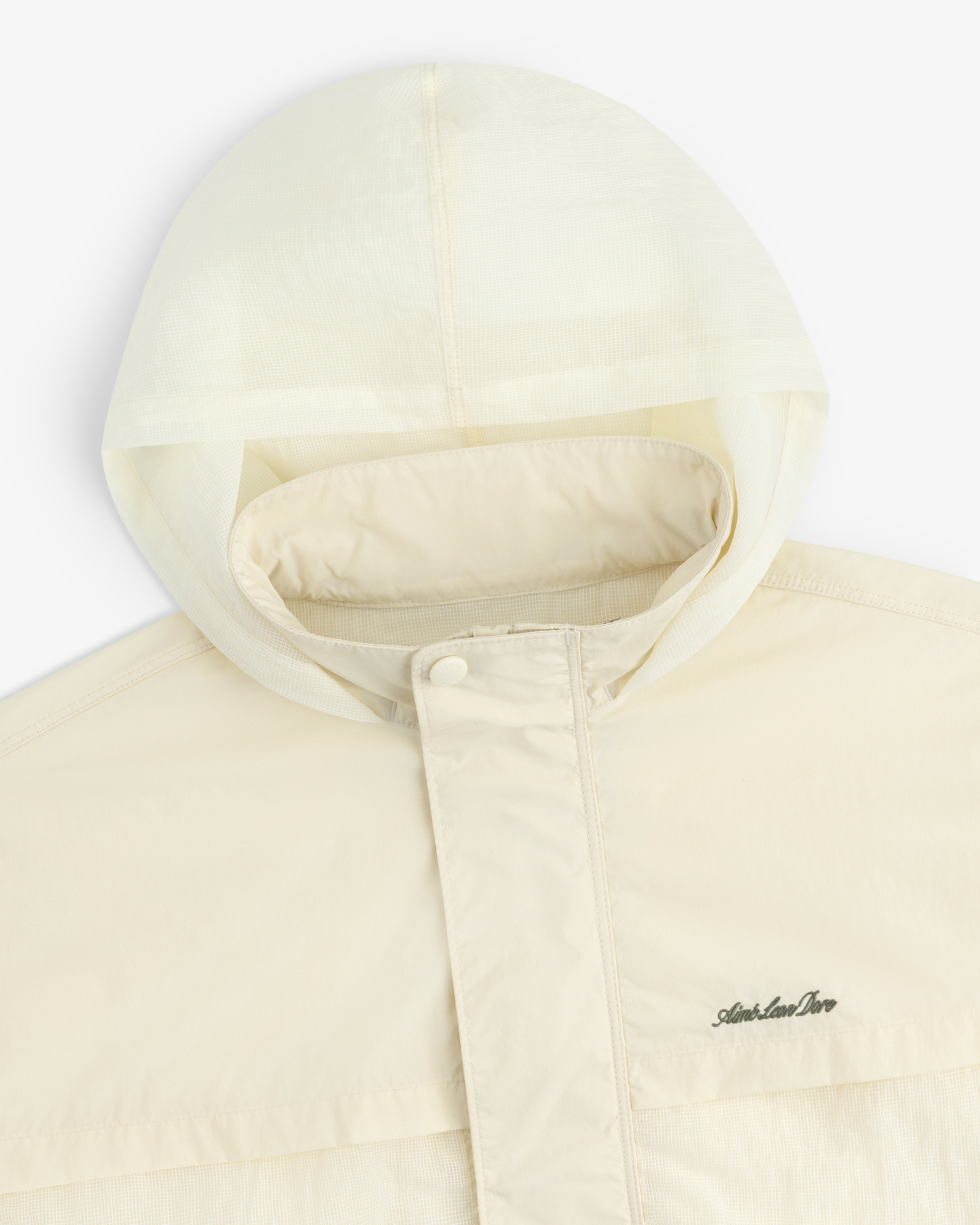 Cream nylon track jacket with hood, snap-button flap, and subtle embroidered chest logo.