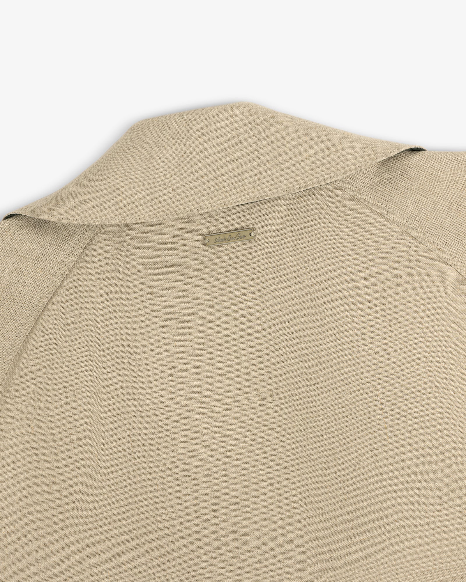 Close-up of the back collar and shoulder of the Linen Trench Coat in beige textured fabric with a small metal nameplate.