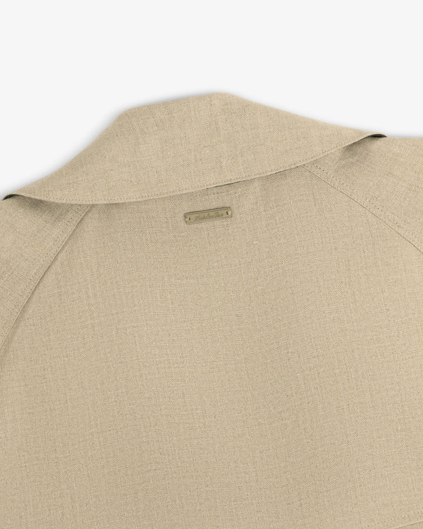 Close-up of the back collar and shoulder of the Linen Trench Coat in beige textured fabric with a small metal nameplate.