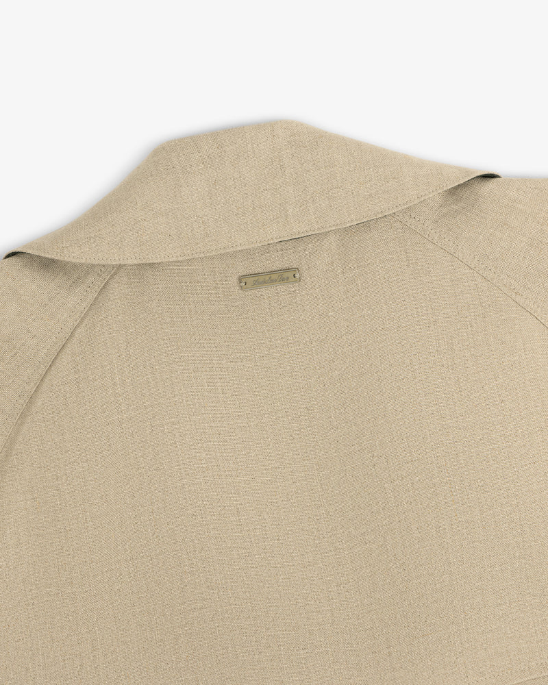 Close-up of the back collar and shoulder of the Linen Trench Coat in beige textured fabric with a small metal nameplate.