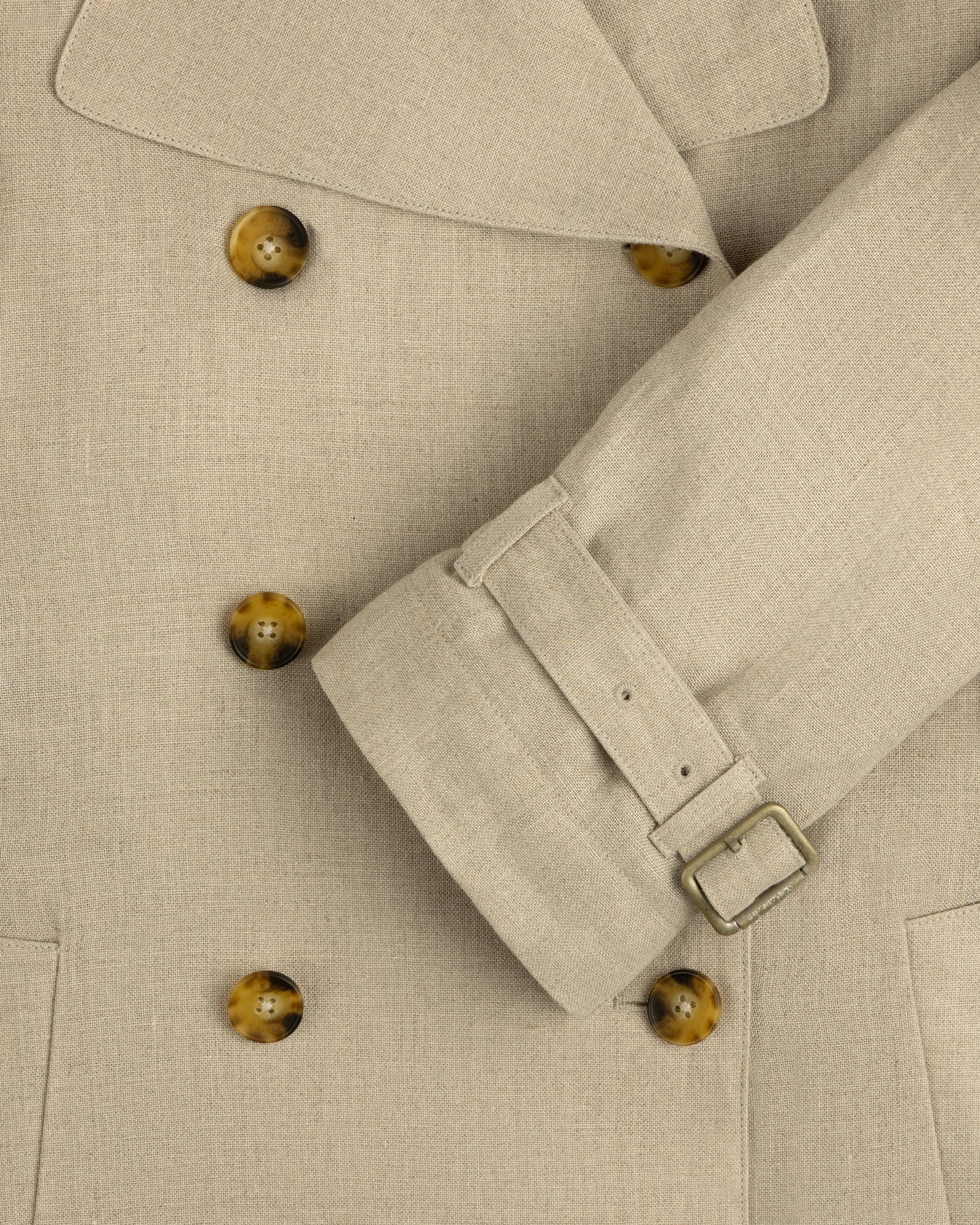 Close-up of Linen Trench Coat with brown buttons and belted cuff, highlighting the detailed fabric texture.