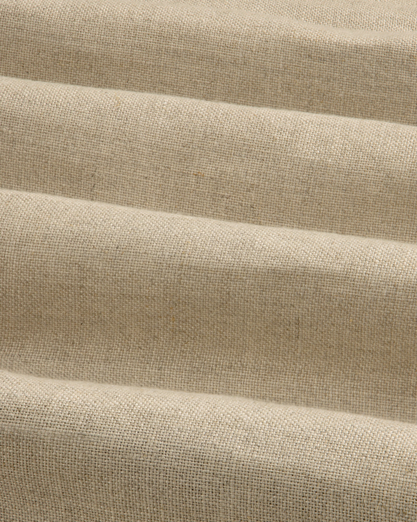 The Linen Trench Coat features beige, textured fabric with horizontal, wavy folds for a dynamic light and shadow effect.