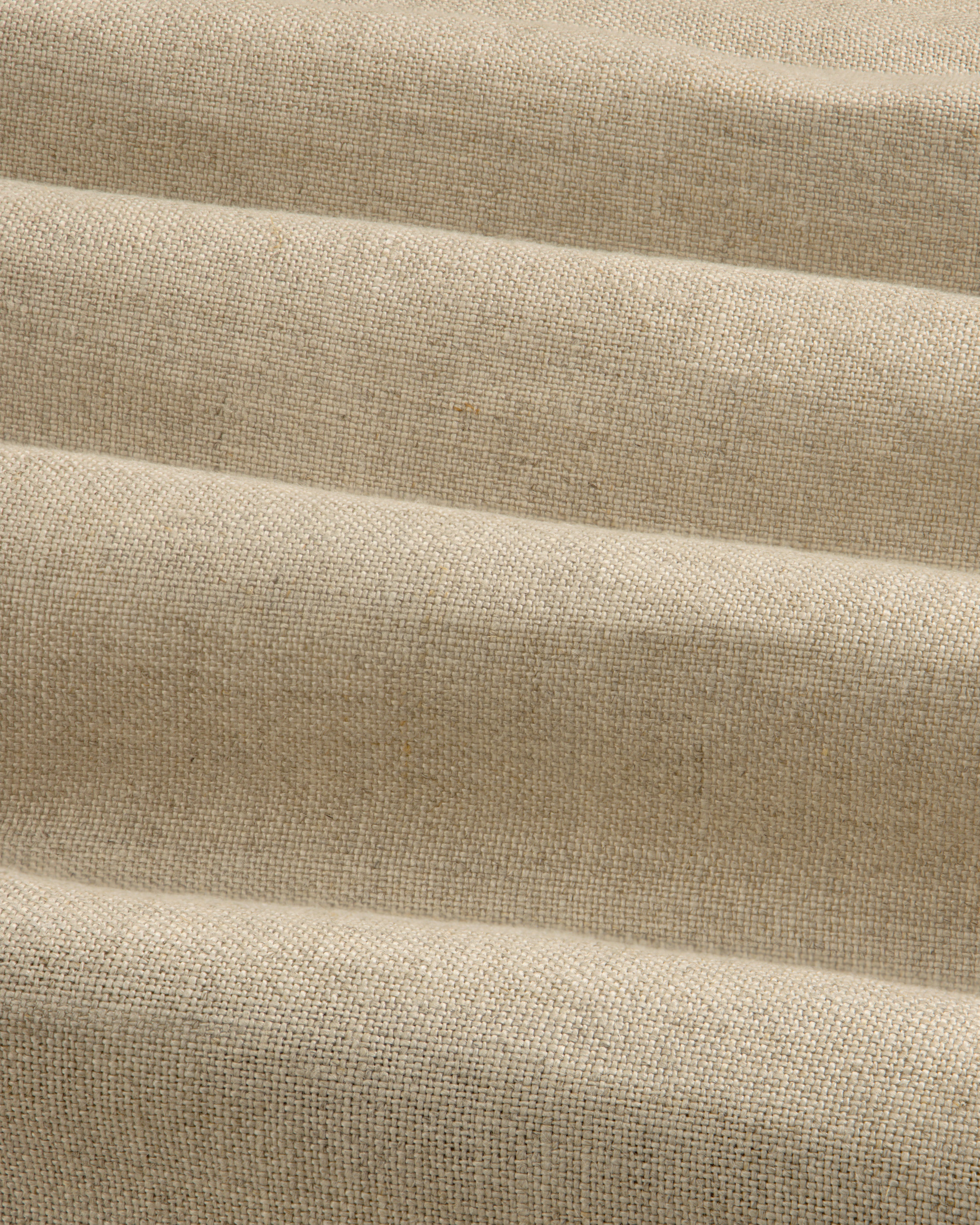 The Linen Trench Coat features beige, textured fabric with horizontal, wavy folds for a dynamic light and shadow effect.