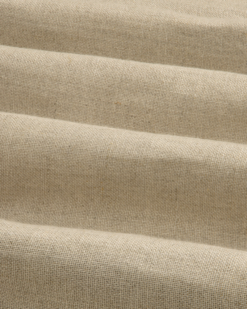 The Linen Trench Coat features beige, textured fabric with horizontal, wavy folds for a dynamic light and shadow effect.