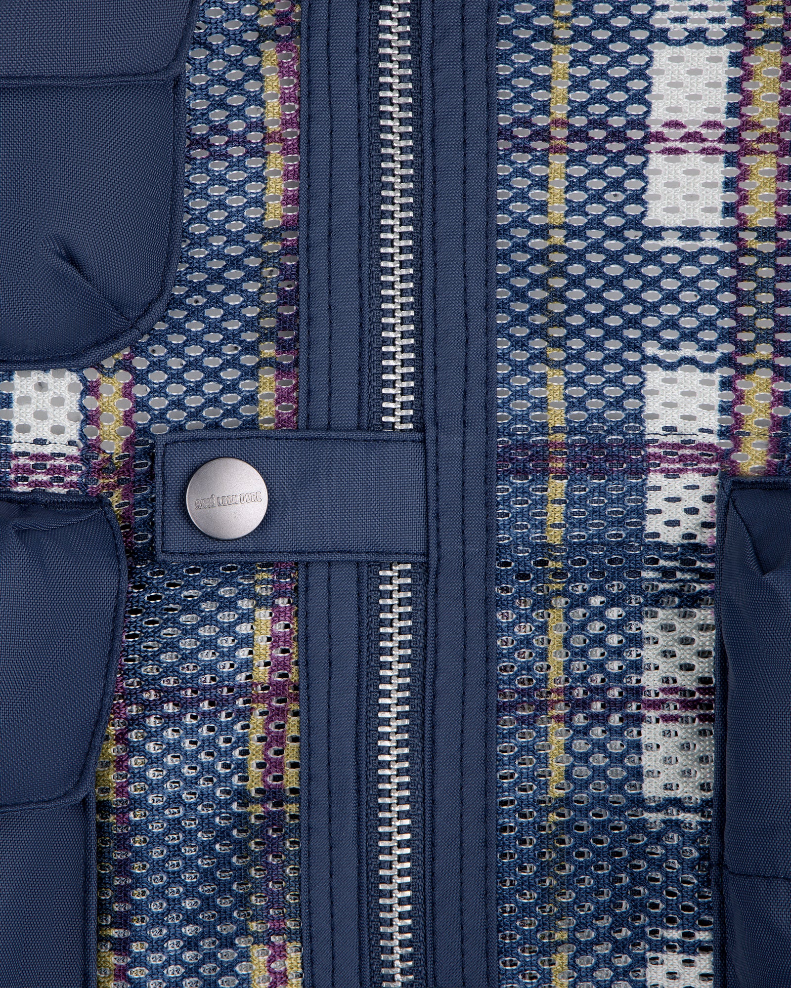 Close-up of blue zipper and snap button on Nylon Madras Utility Vest with multicolored grid and mesh pattern.
