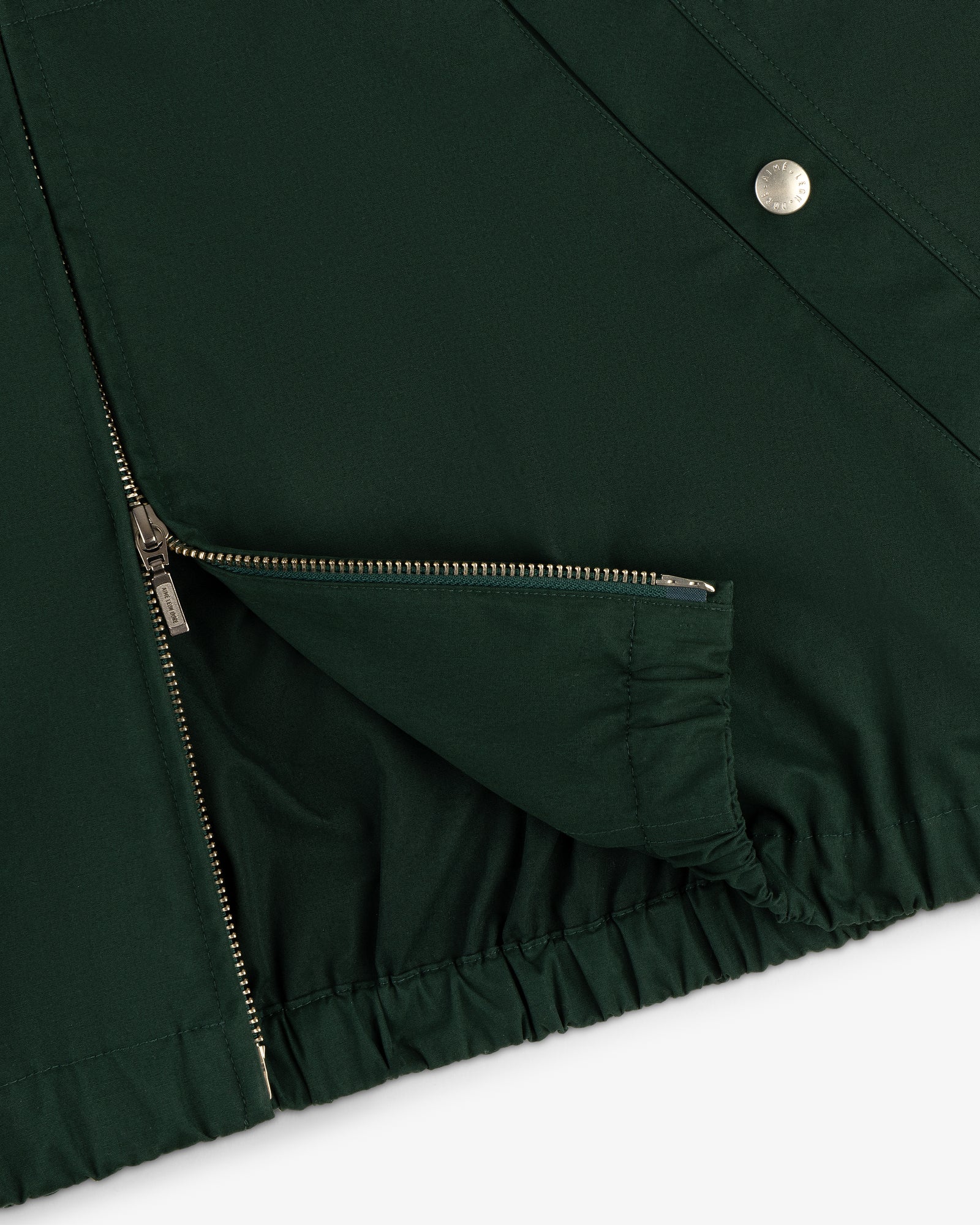 Close-up of Micro Logo Lightweight Jacket in dark green with silver zipper, snap fastener, and elastic hem on white background.