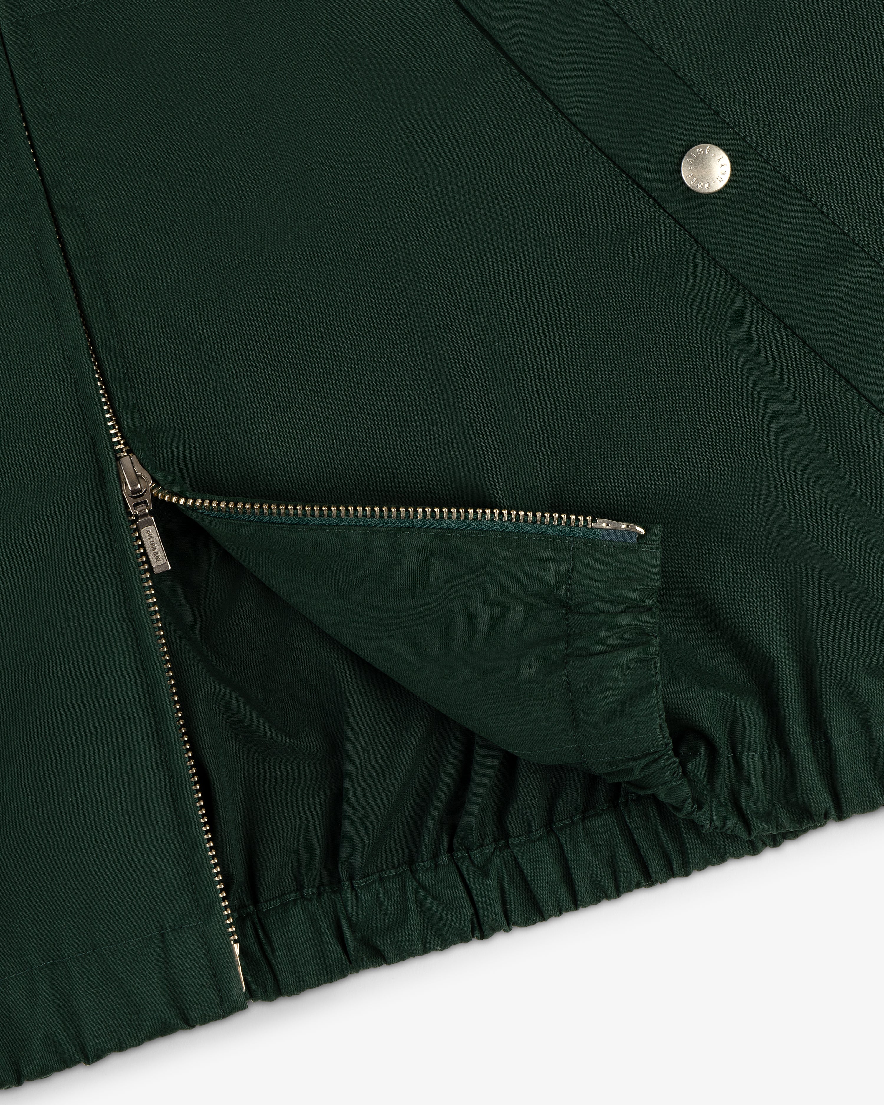Close-up of Micro Logo Lightweight Jacket in dark green with silver zipper, snap fastener, and elastic hem on white background.