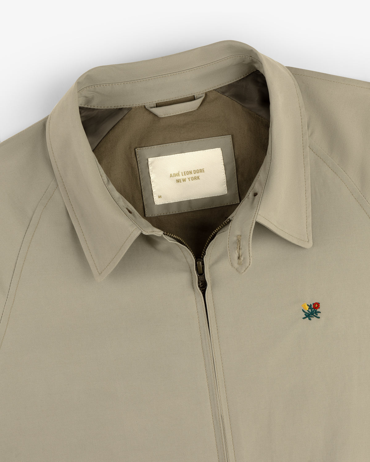 Beige Crest Casual Jacket with collar, zip-up front, small floral embroidery, and inside "Aimé Leon Dore New York" label.