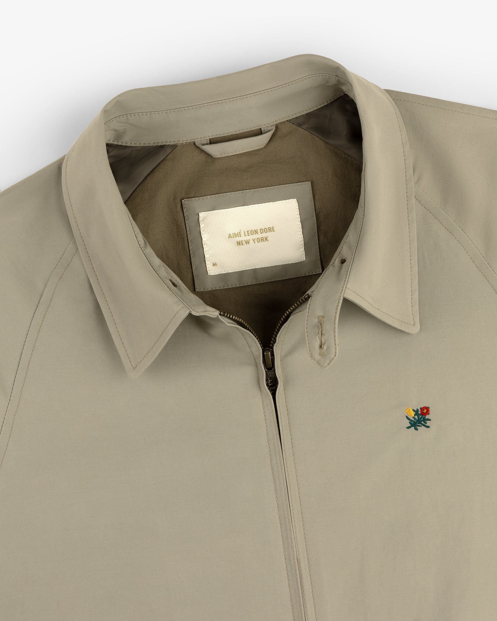 Beige Crest Casual Jacket with collar, zip-up front, small floral embroidery, and inside "Aimé Leon Dore New York" label.
