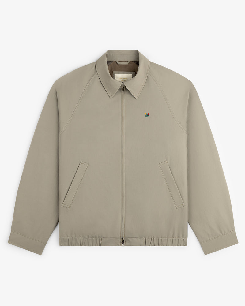 Crest Casual Jacket: light beige zip-up with collar, two slanted pockets, and small chest logo.