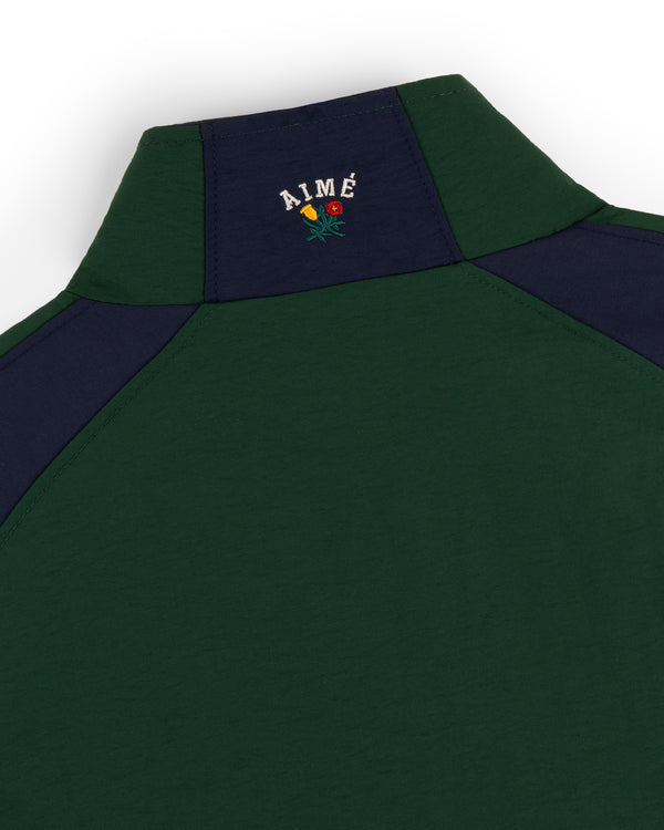 Close-up of Crest Nylon Half-Zip Pullover in green/navy, featuring AIMÉ and a small floral embroidery on the back.
