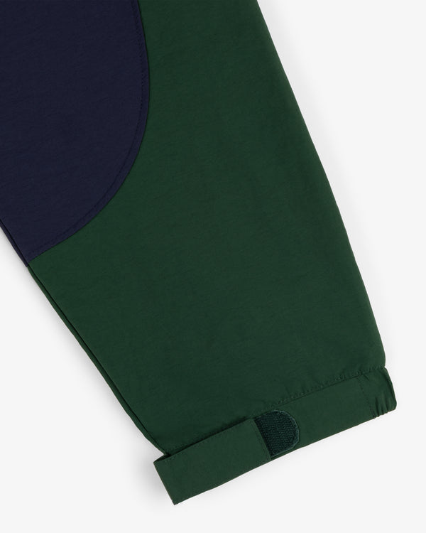 A close-up of the Crest Nylon Half-Zip Pullover shows a green pant leg with navy patch and adjustable Velcro cuff.