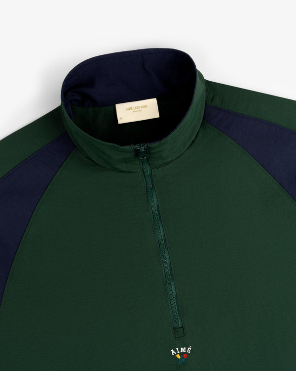 Dark green Crest Nylon Half-Zip Pullover with navy collar, sleeves, and AIMÉ embroidered on the front.