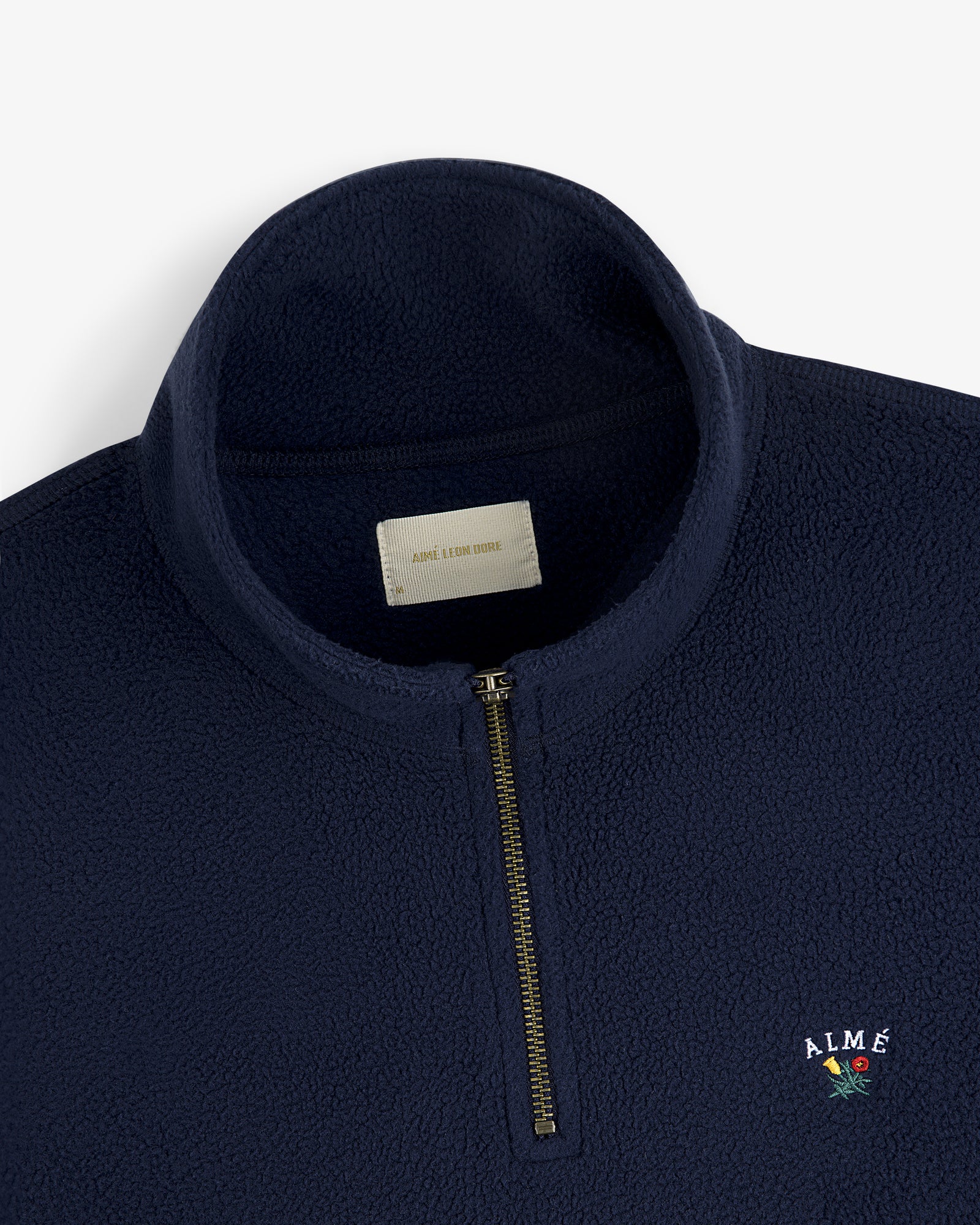 Crest Quarter-Zip Fleece Pullover in navy blue with gold zipper and ALMÉ embroidered in a small floral design.