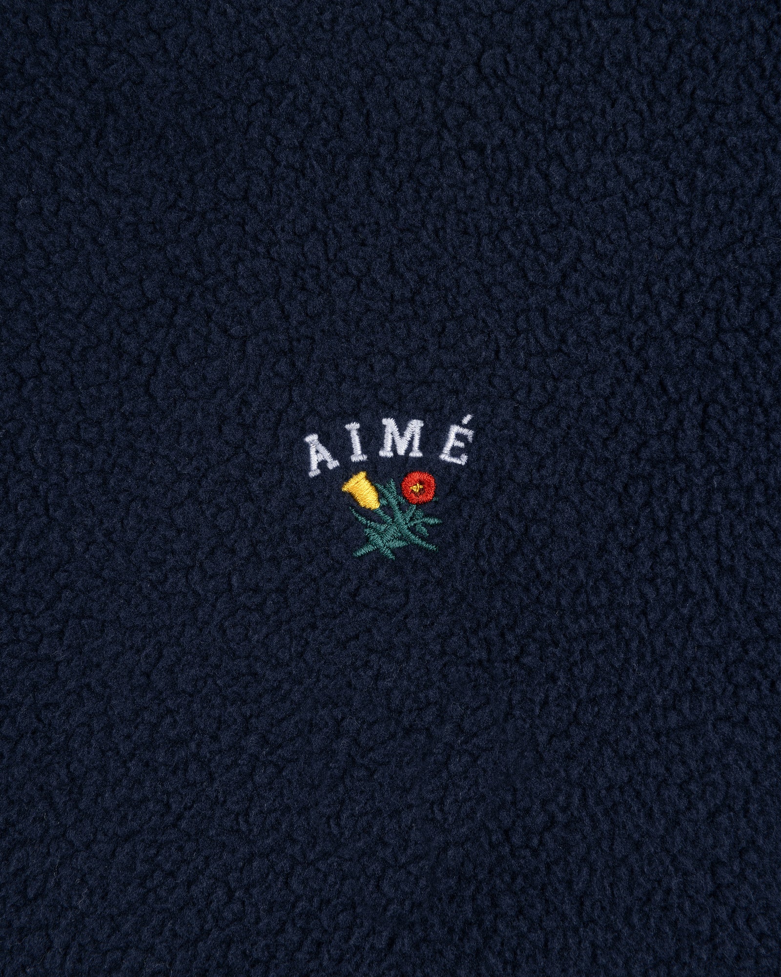 Navy blue Crest Quarter-Zip Fleece Pullover with AIMÉ embroidered above a yellow and red flower.