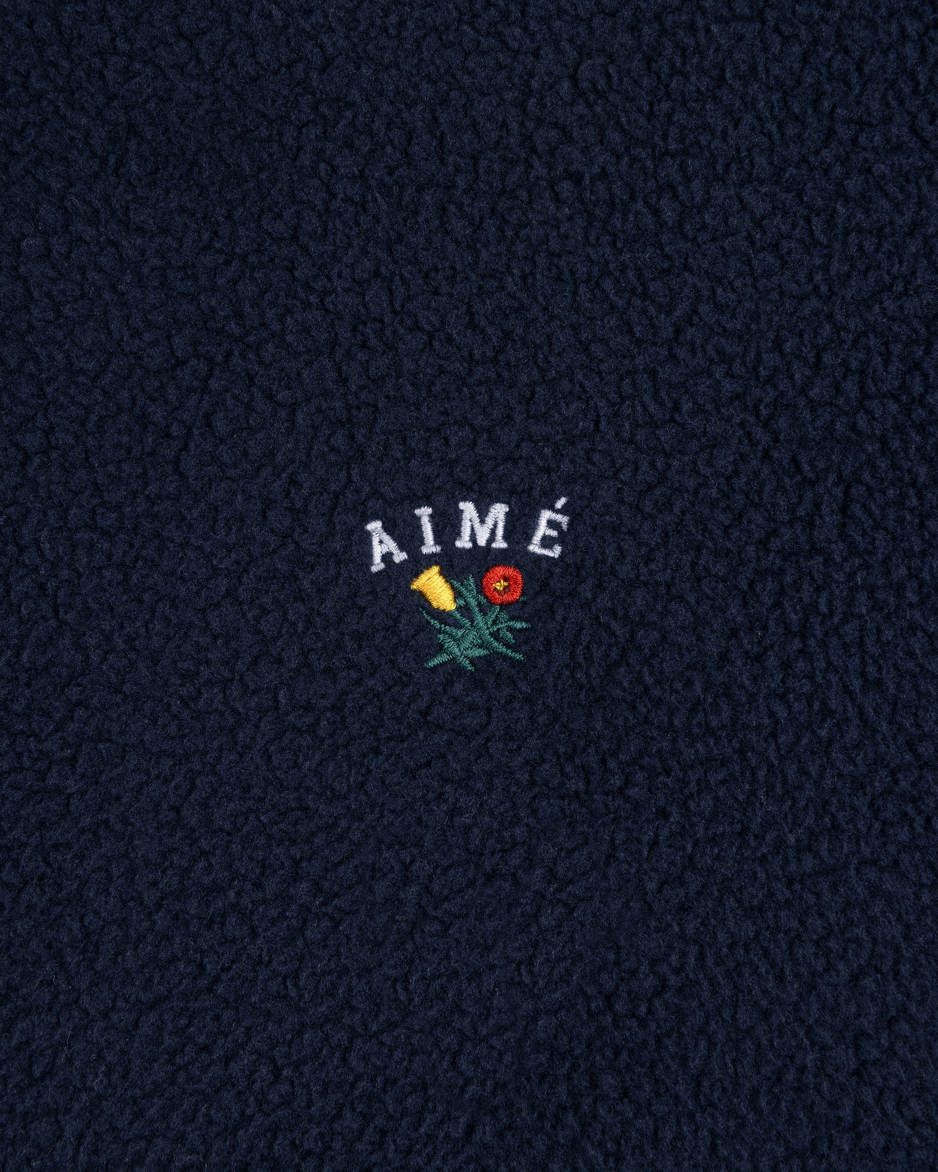 Navy blue Crest Quarter-Zip Fleece Pullover with AIMÉ embroidered above a yellow and red flower.