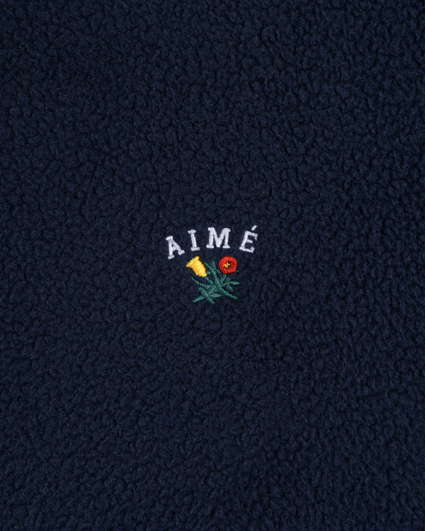 Navy blue Crest Quarter-Zip Fleece Pullover with AIMÉ embroidered above a yellow and red flower.