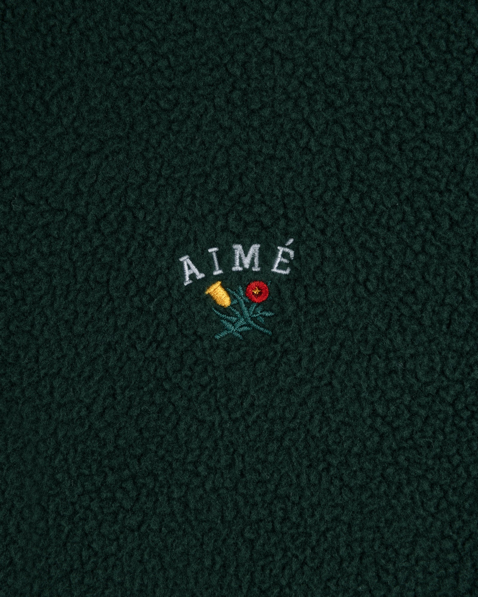 Crest Quarter-Zip Fleece Pullover in dark green with AIMÉ embroidered above a yellow and red flower.