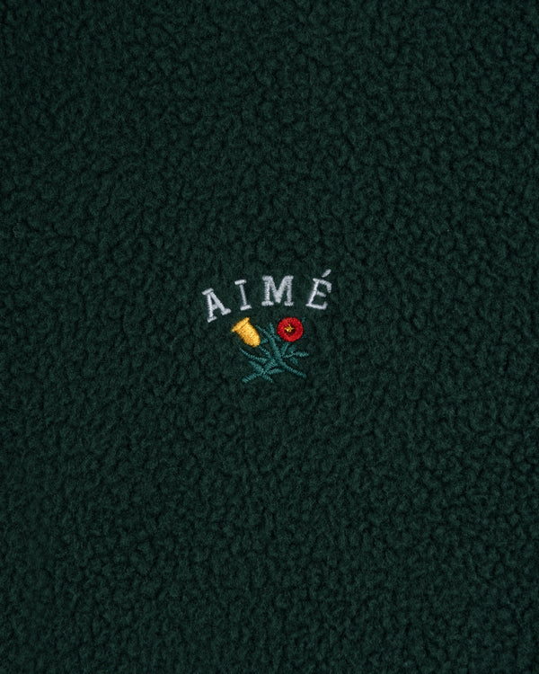 Crest Quarter-Zip Fleece Pullover in dark green with AIMÉ embroidered above a yellow and red flower.