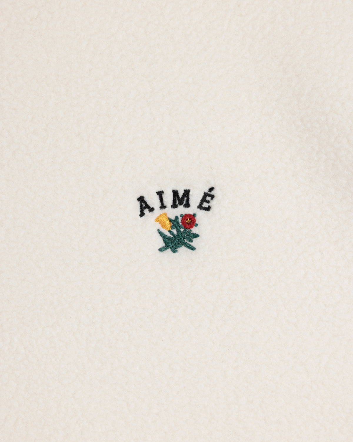 Crest Quarter-Zip Fleece Pullover with AIMÉ text and a small yellow and red flower embroidered on white fleece.