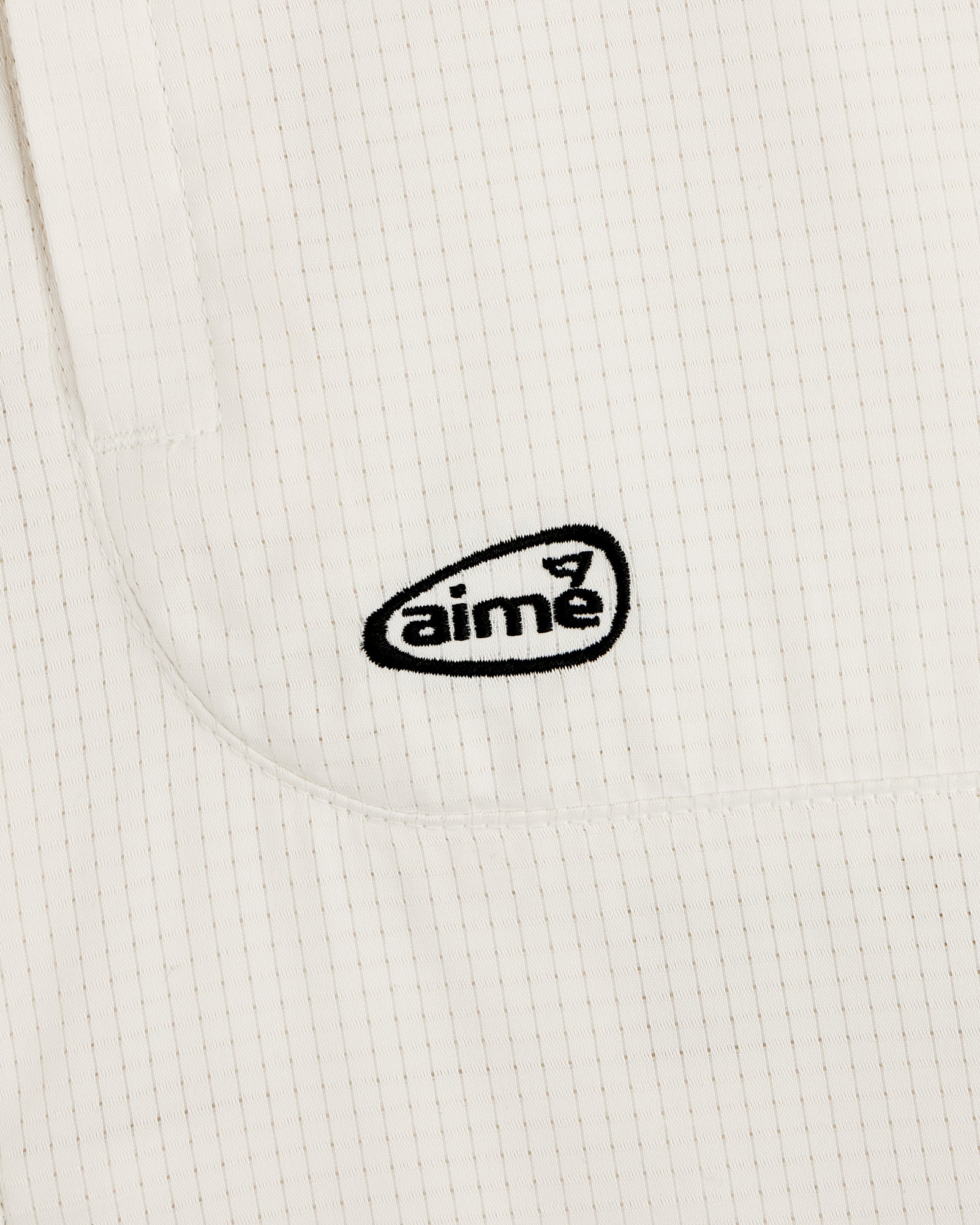 Close-up of the ALD Golf Lightweight Tips Windbreaker’s white, textured fabric with thin stripes and black aime logo.