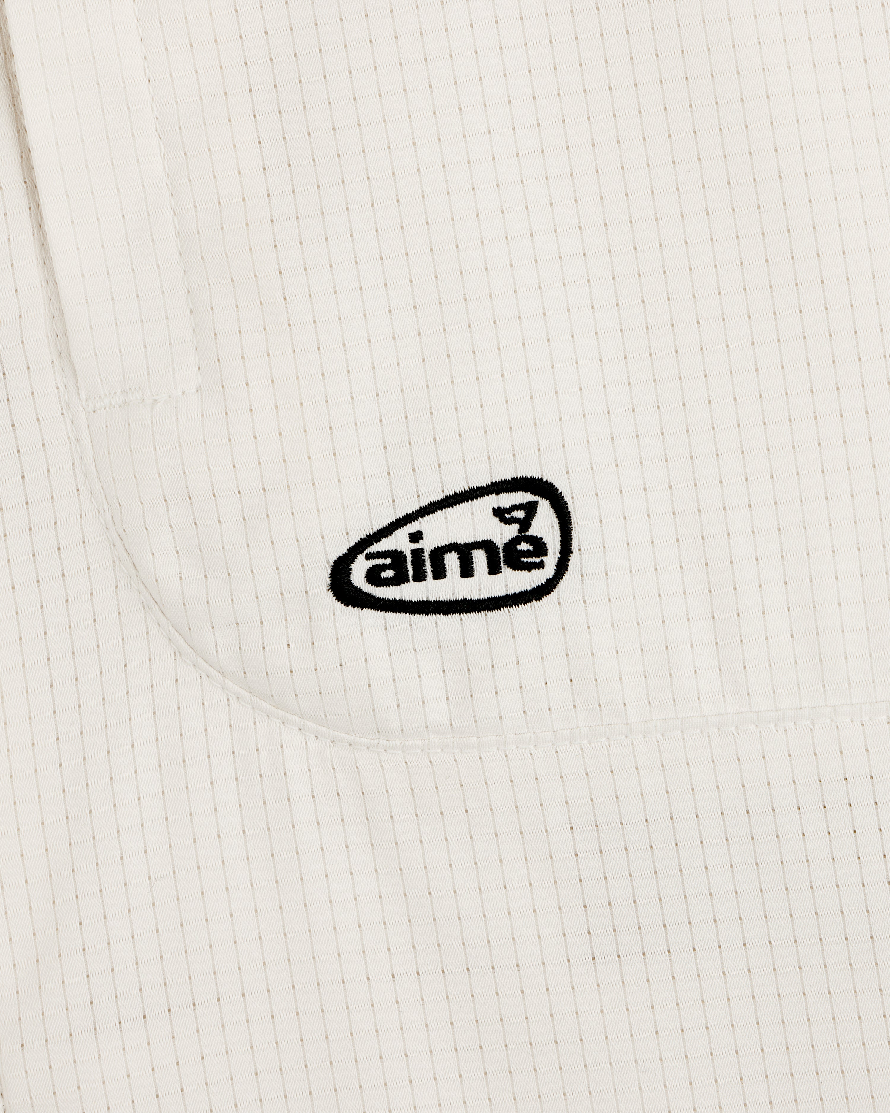 Close-up of the ALD Golf Lightweight Tips Windbreaker’s white, textured fabric with thin stripes and black aime logo.