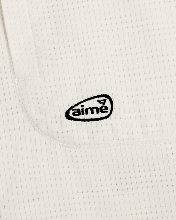 Close-up of the ALD Golf Lightweight Tips Windbreaker’s white, textured fabric with thin stripes and black aime logo.