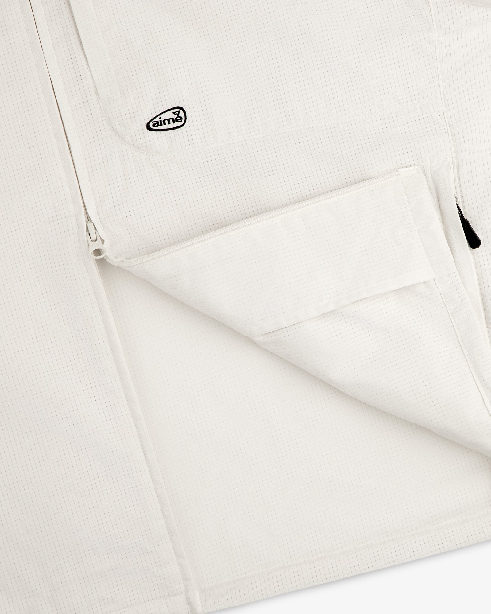 Close-up of the ALD Golf Lightweight Tips Windbreaker, featuring a zip pocket and small Aimé logo patch near the zipper.