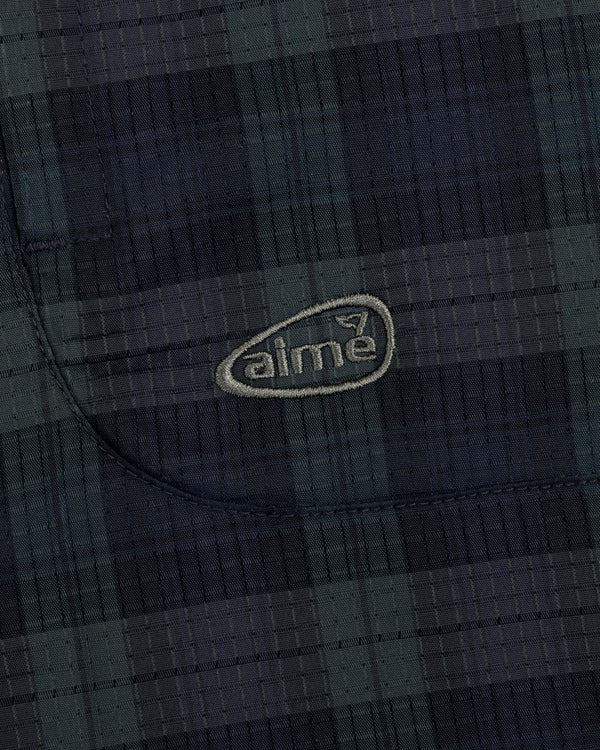 Close-up of ALD Golf Lightweight Tips Windbreaker showing dark plaid fabric, stitched pocket, and light aime logo.