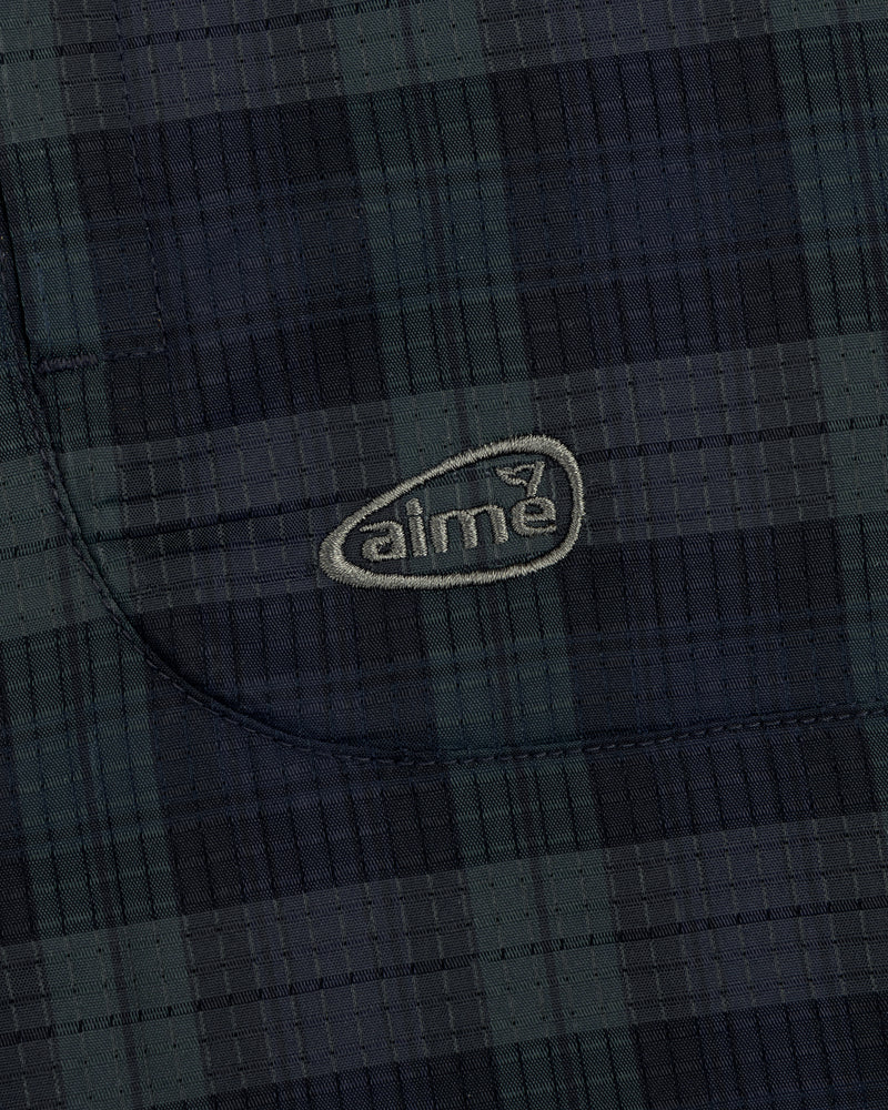 Close-up of ALD Golf Lightweight Tips Windbreaker showing dark plaid fabric, stitched pocket, and light aime logo.