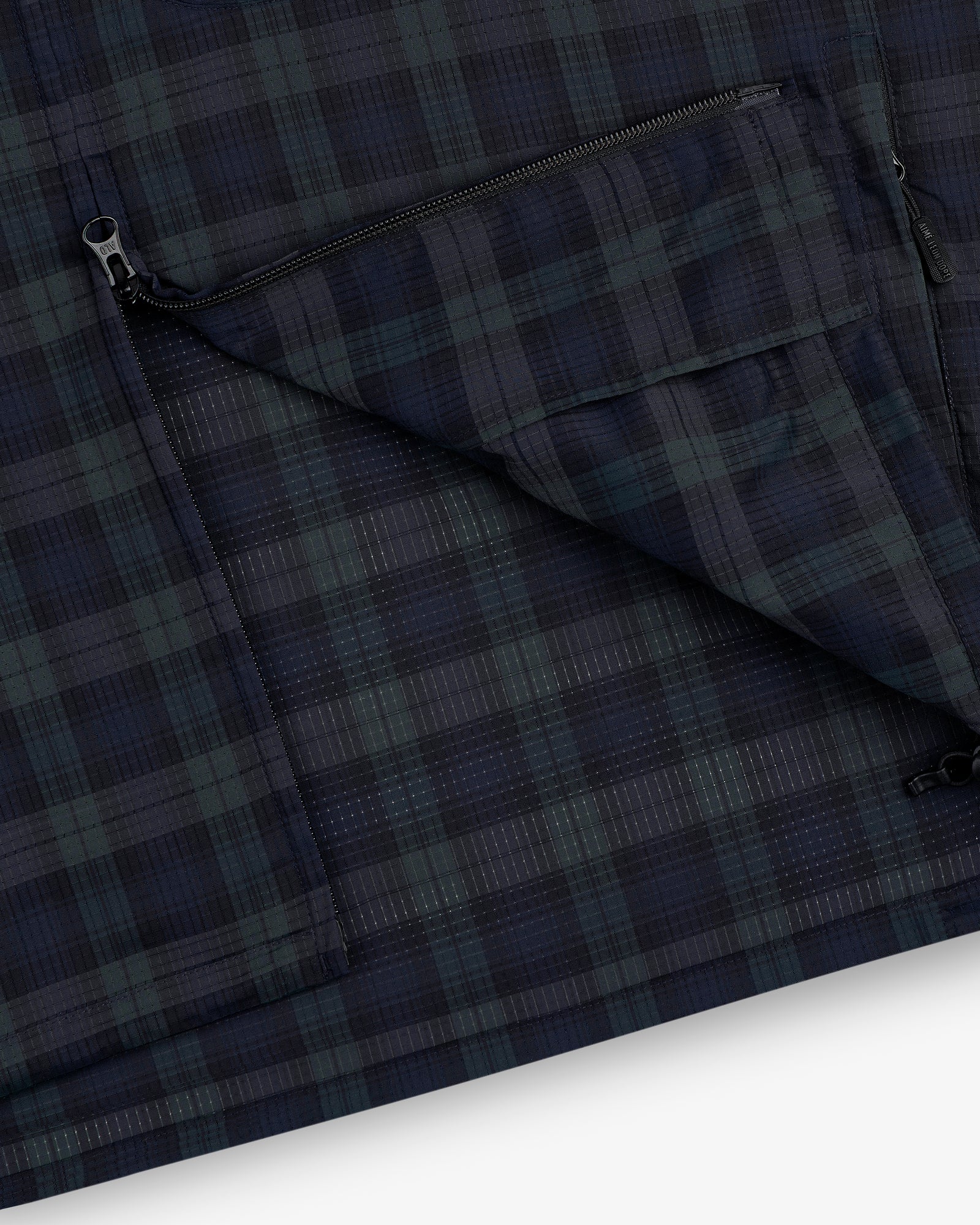 Close-up of the ALD Golf Lightweight Tips Windbreaker in navy and green plaid with a zippered pocket and visible stitching.