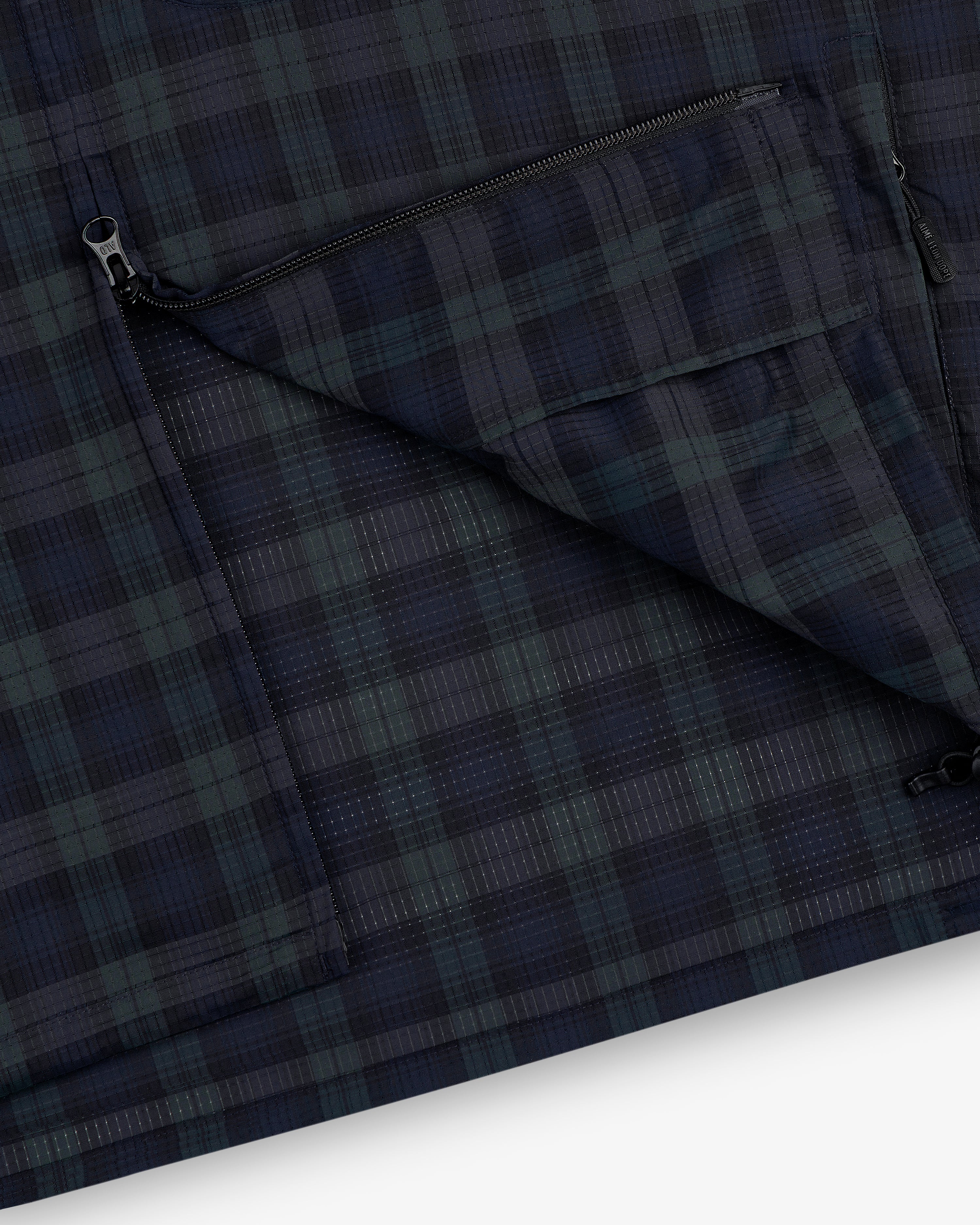 Close-up of the ALD Golf Lightweight Tips Windbreaker in navy and green plaid with a zippered pocket and visible stitching.