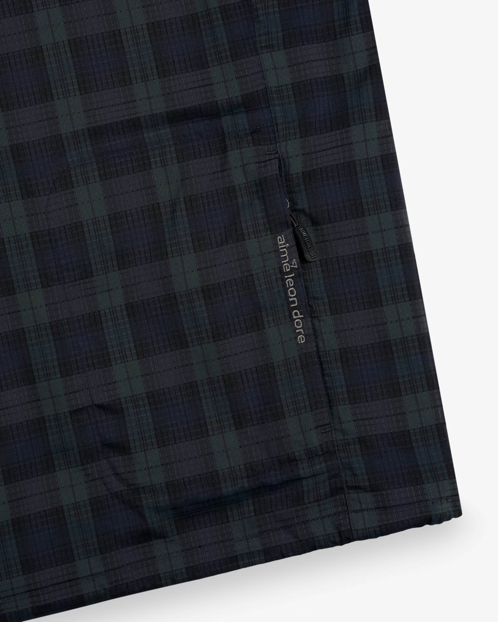 Close-up of ALD Golf Lightweight Tips Windbreaker in dark green and navy plaid with a small label near the seam.