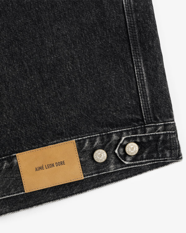 Close-up of AIMÉ LEON DORE label and silver buttons on black Denim Trucker Jacket.