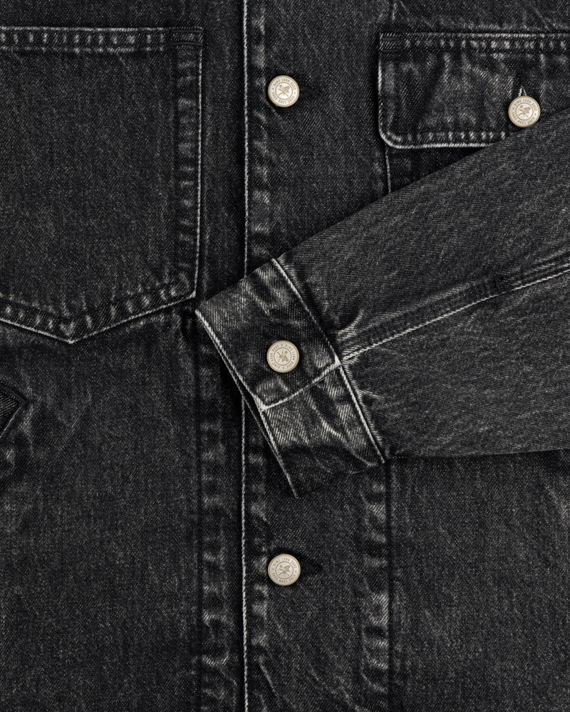 Close-up of a Denim Trucker Jacket in black with silver buttons, chest pockets, and one sleeve across the front.