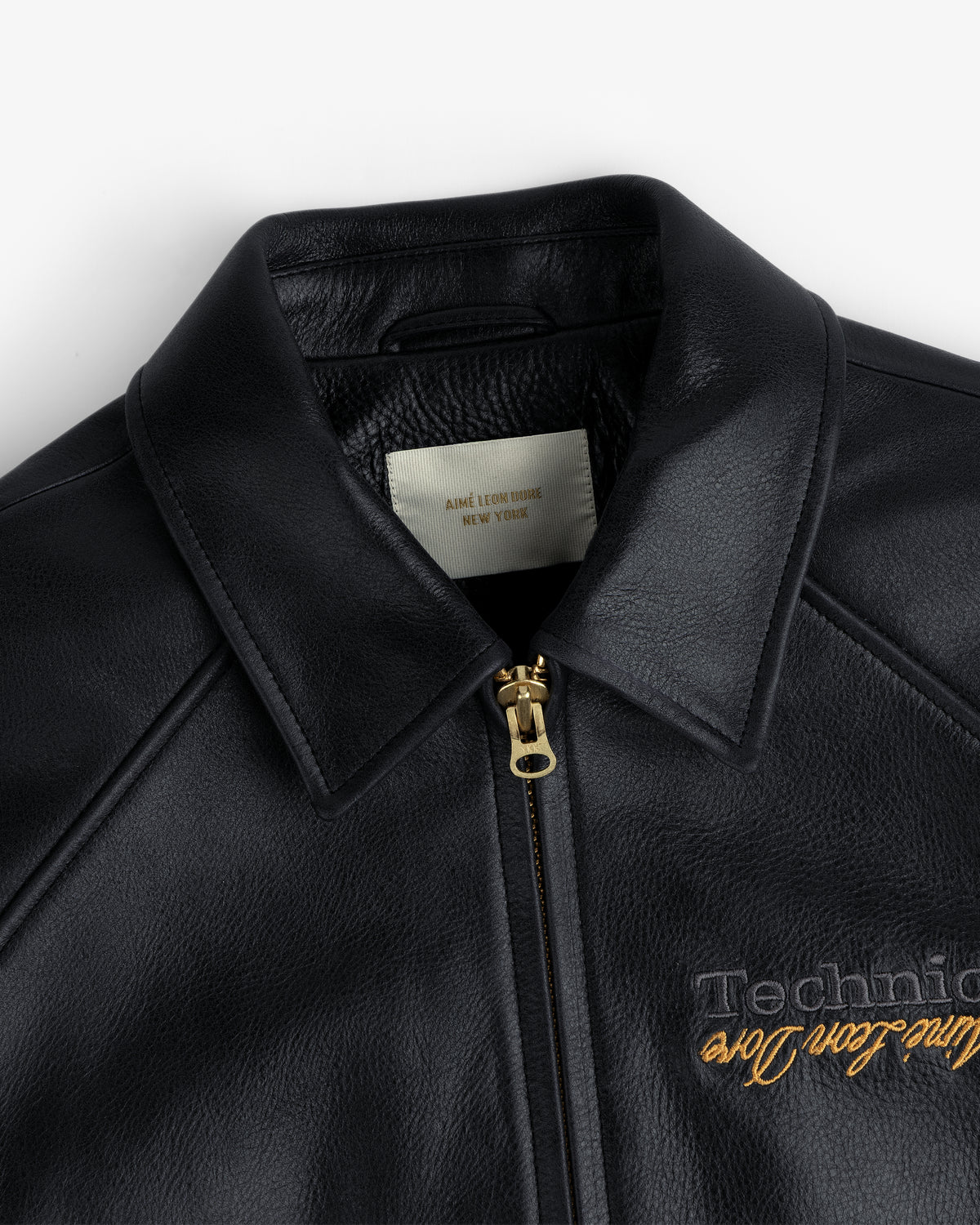 Close-up of the ALD / Technics Varsity Leather Jacket in black leather with gold zipper, showing collar and label.