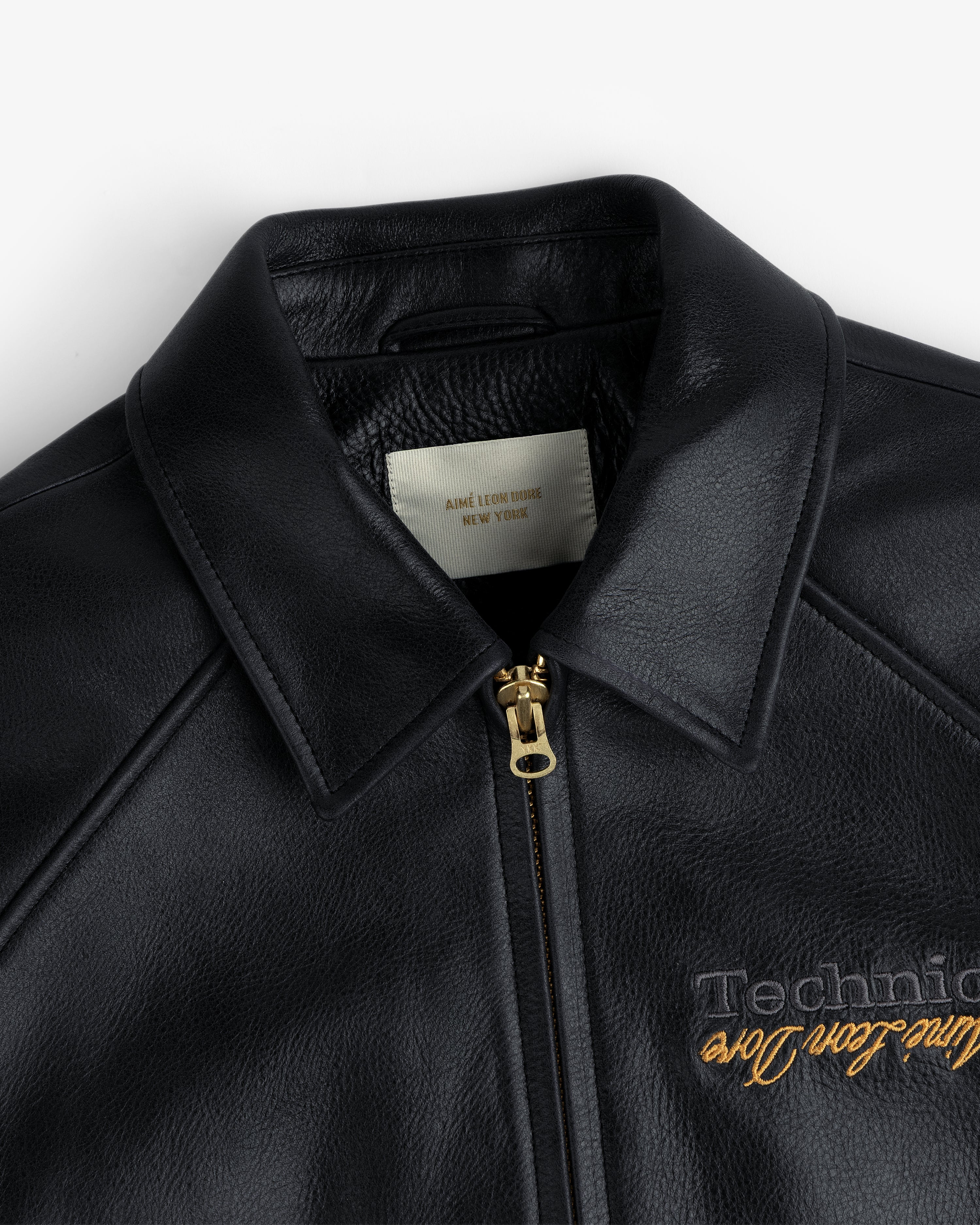 Close-up of the ALD / Technics Varsity Leather Jacket in black leather with gold zipper, showing collar and label.