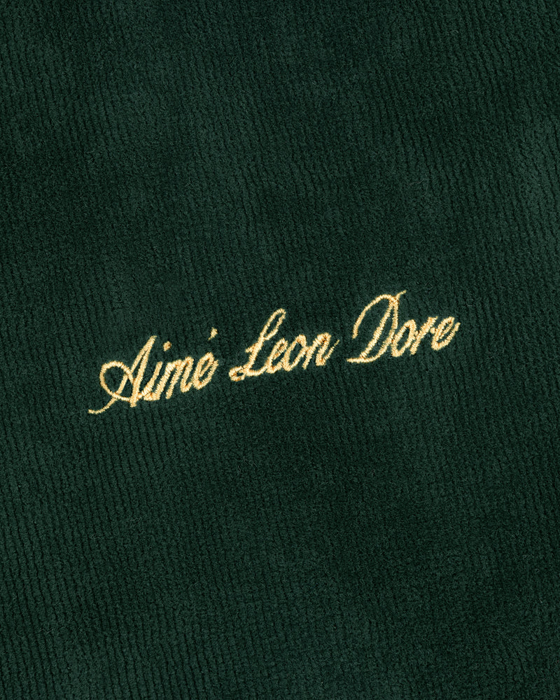 Gold script text Aimé Leon Dore embroidered on dark green ribbed Mulberry Robe fabric.