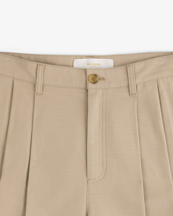 Close-up of Double Pleated Pant in beige with a brown button and belt loops at the waistband.