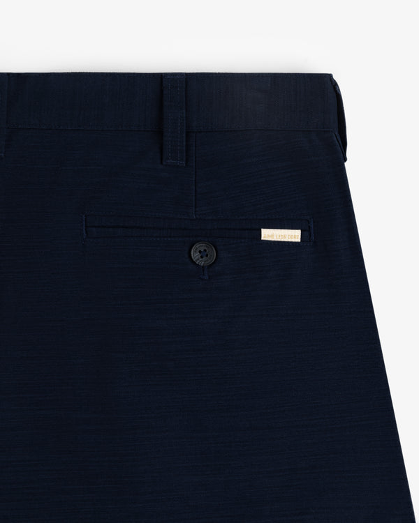 Close-up of Double Pleated Pant in navy blue with back pocket, button, belt loop, and a small white label above the pocket.