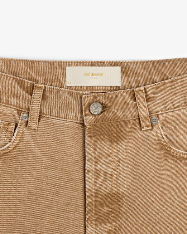 Close-up of tan Relaxed Fit 5-Pocket Denim Pant with button, belt loops, and white Aime Leon Dore label on waistband.