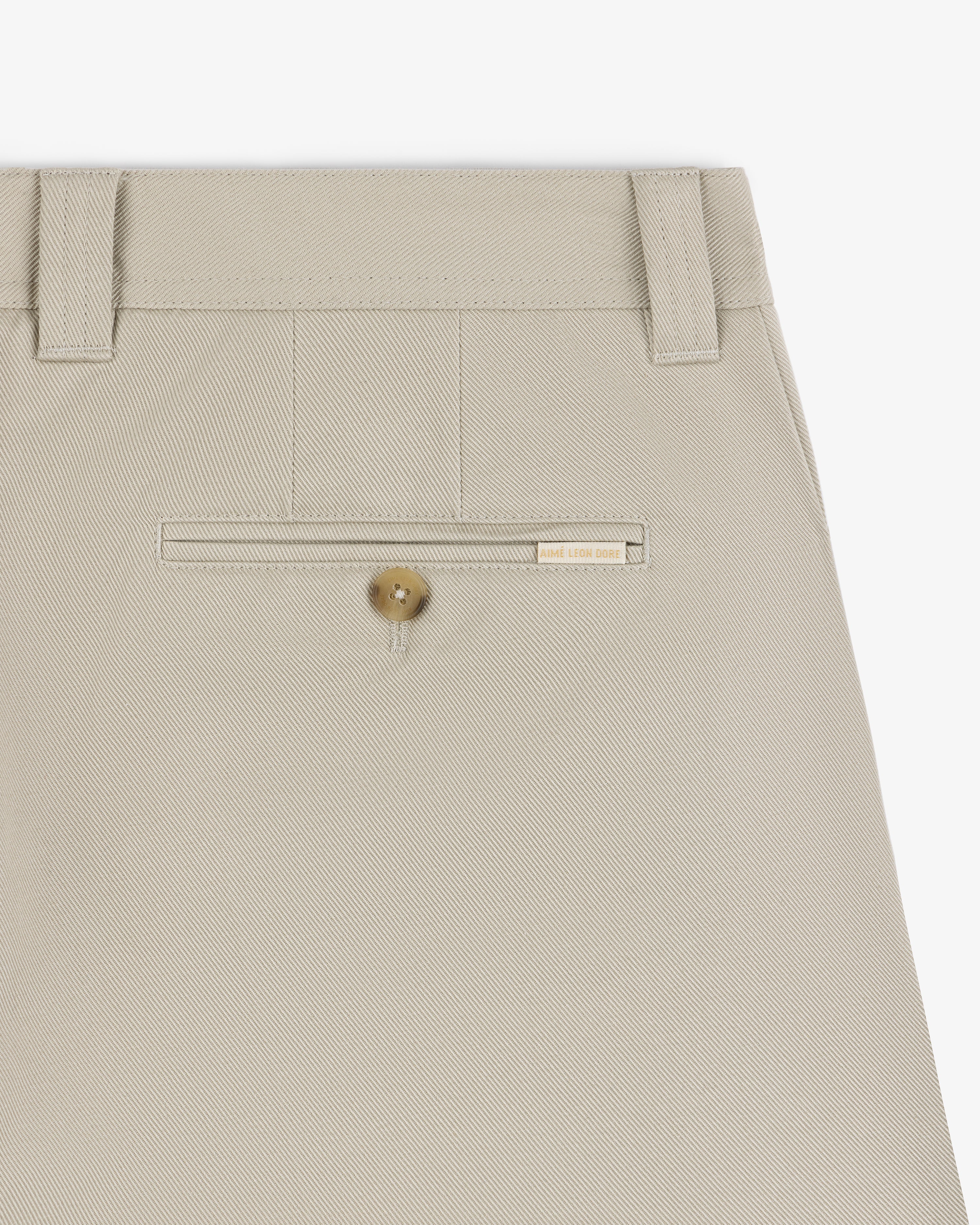 Close-up of Officer Pant in beige showing a back welt pocket with button and a small beige label above it.