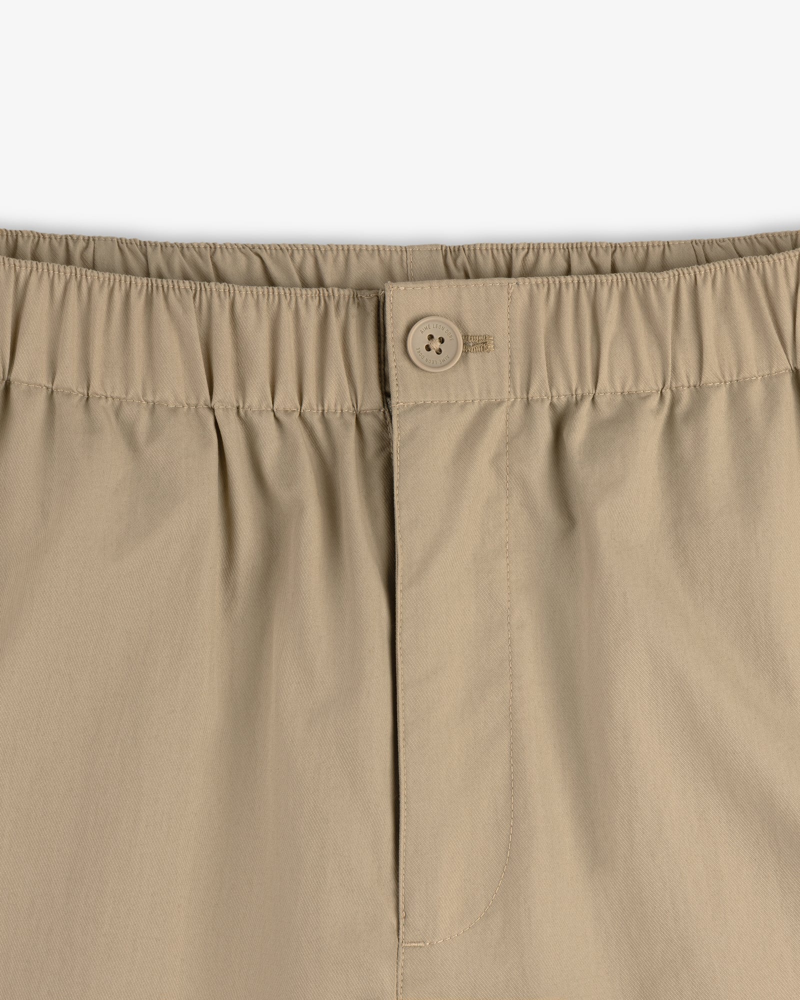 Close-up of Relaxed Cotton Trouser in beige, featuring an elastic waistband, button closure, and front stitched seam.