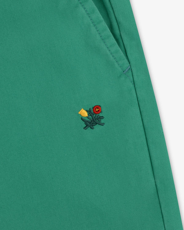 Washed Cotton Windbreaker Pant in green with pocket and small embroidered flower—red center, yellow petals, green stem.